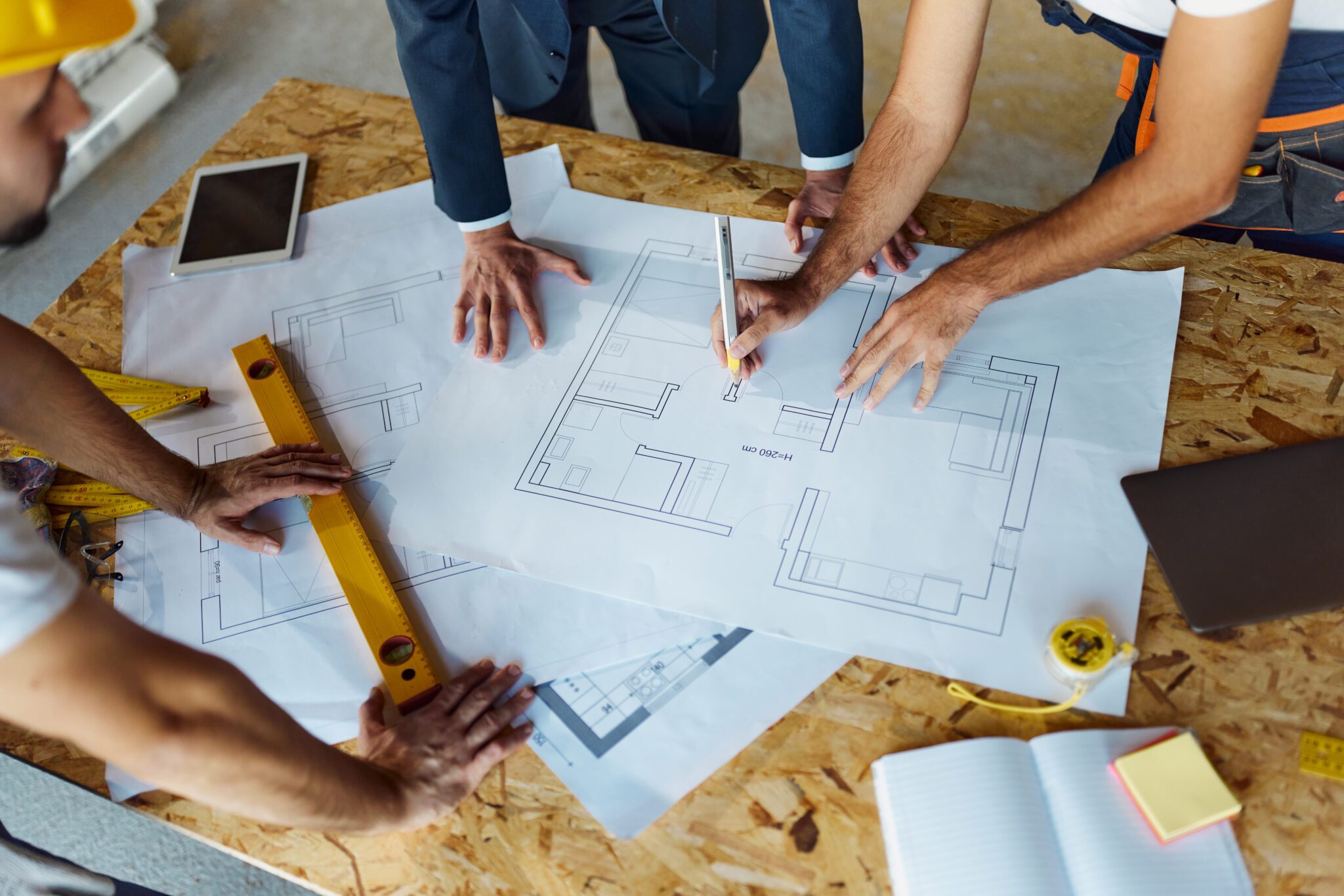 High angle view of unrecognizable foreman and his workers cooperating while drawing on housing plans at construction site.